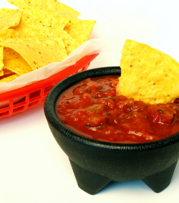 A bowl of nachos next to a bowl of salsa.