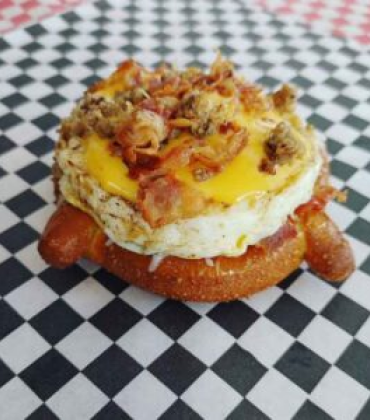 A pretzel with eggs and bacon on top of a checkered tablecloth.