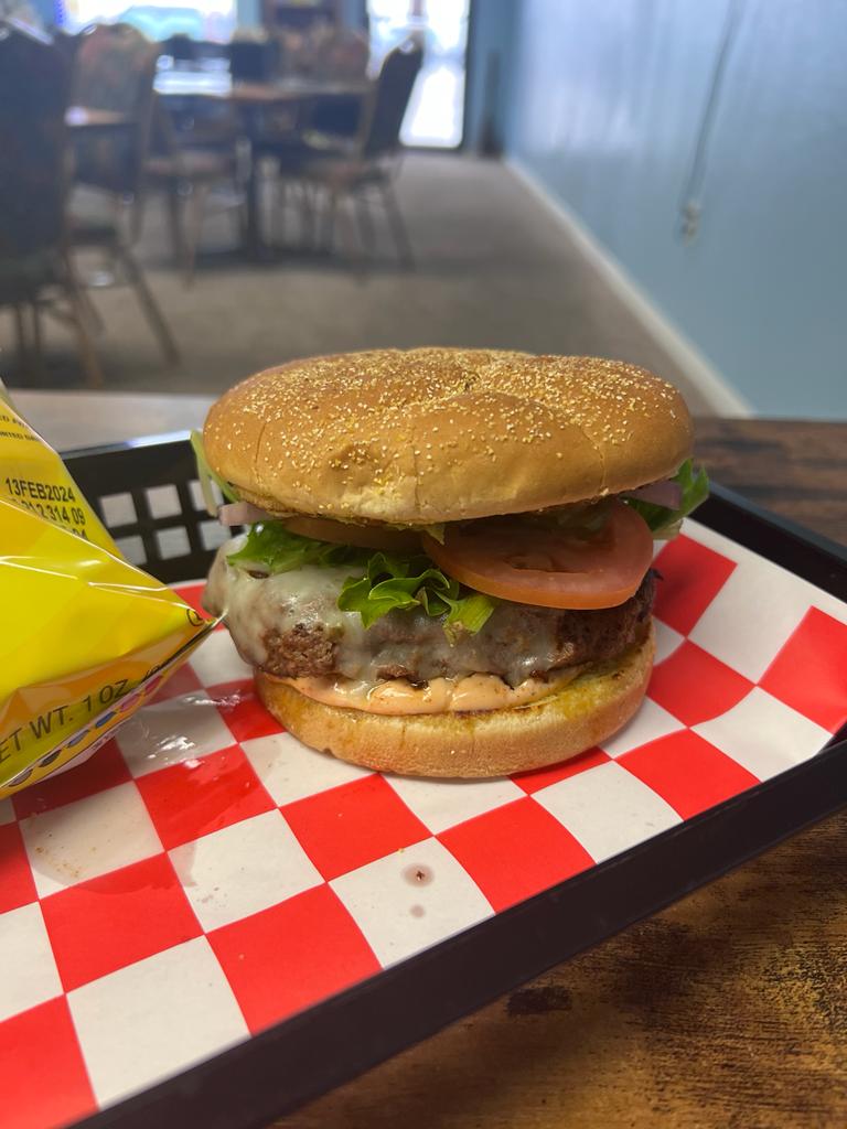 A burger sits on a tray next to a bag of chips.